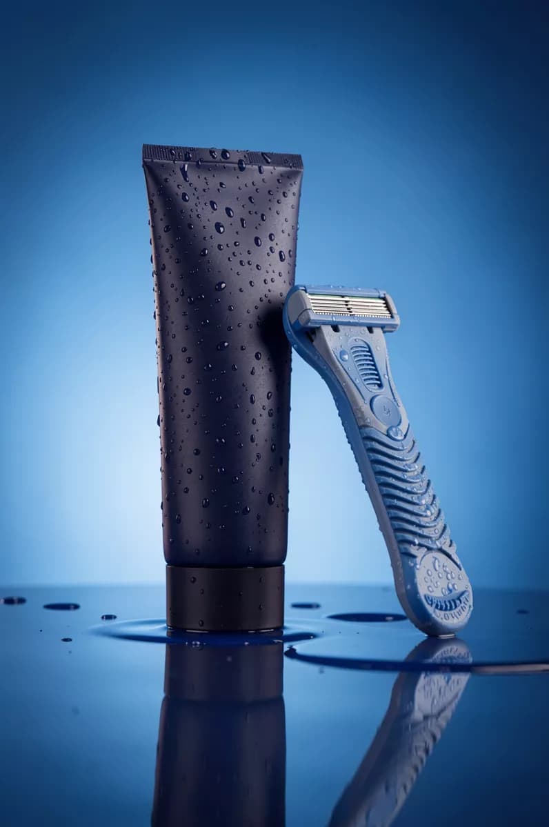 Product and e-commerce: A men's grooming product shot on a wet blue surface: a matte dark navy cosmetic 