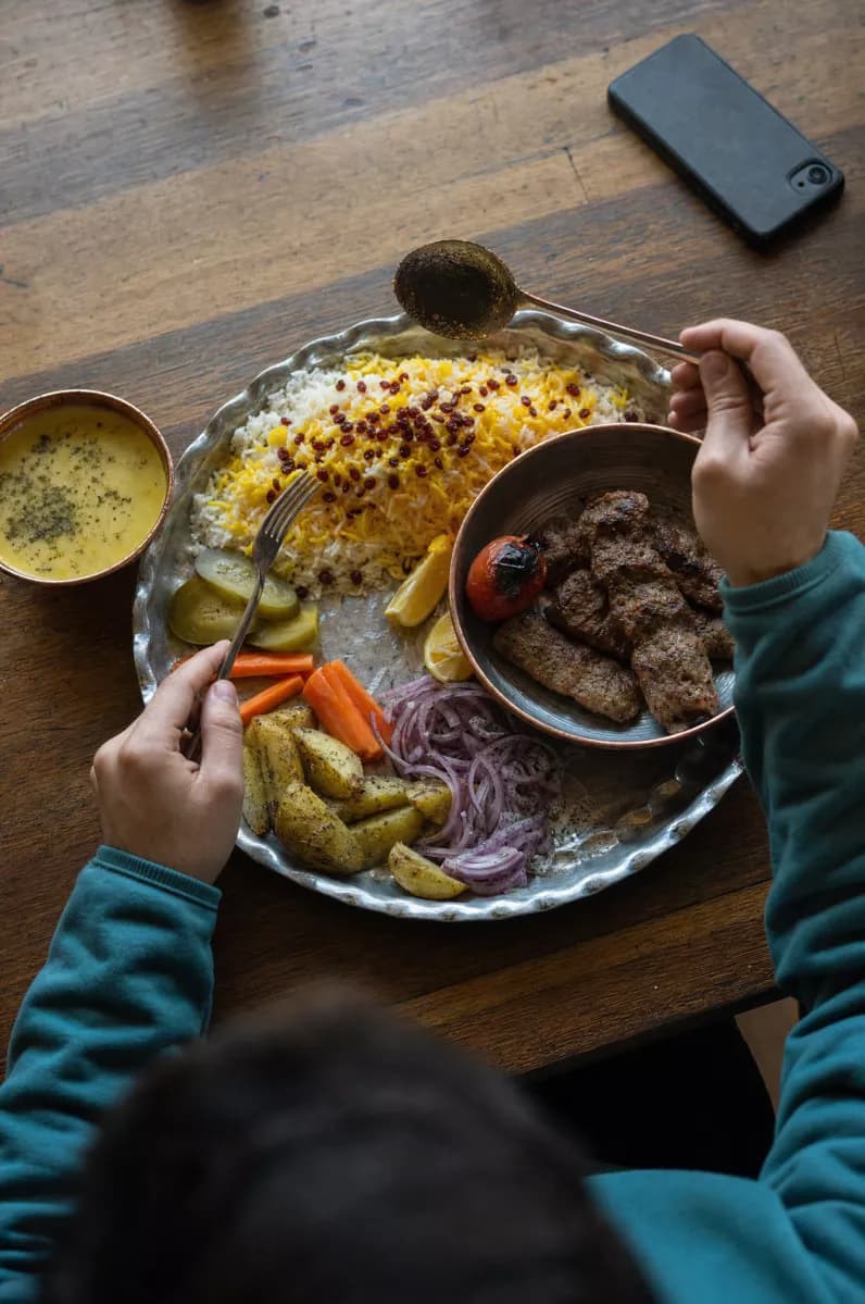 Food and beverage: A Persian meal on a rough wooden table, shot from above at an angle. A large sca