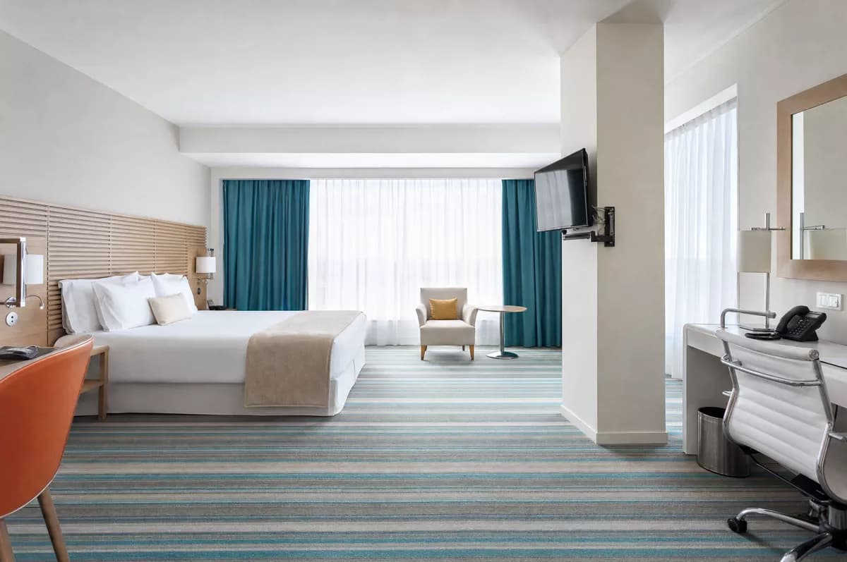 GPT Image 2 — Interior: A spacious modern hotel room. A double bed with a pale wood slatted headboard, c