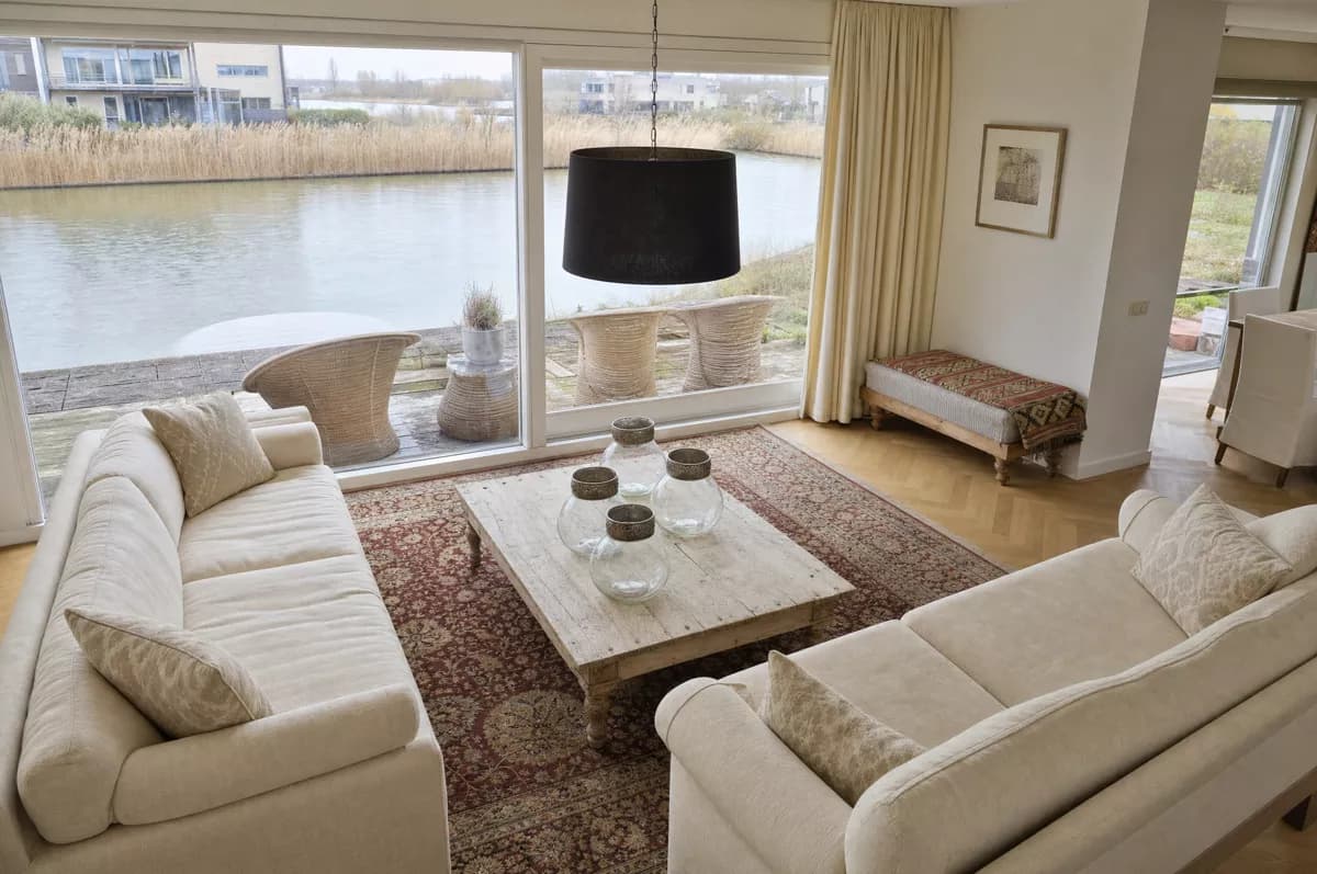 Interior: A bright living room seen from a raised corner viewpoint. Two cream upholstered 