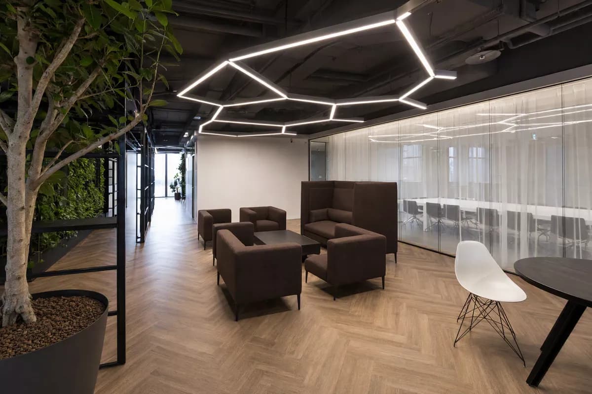 Interior: An open-plan office lounge. Overhead, a large angular ceiling installation of in