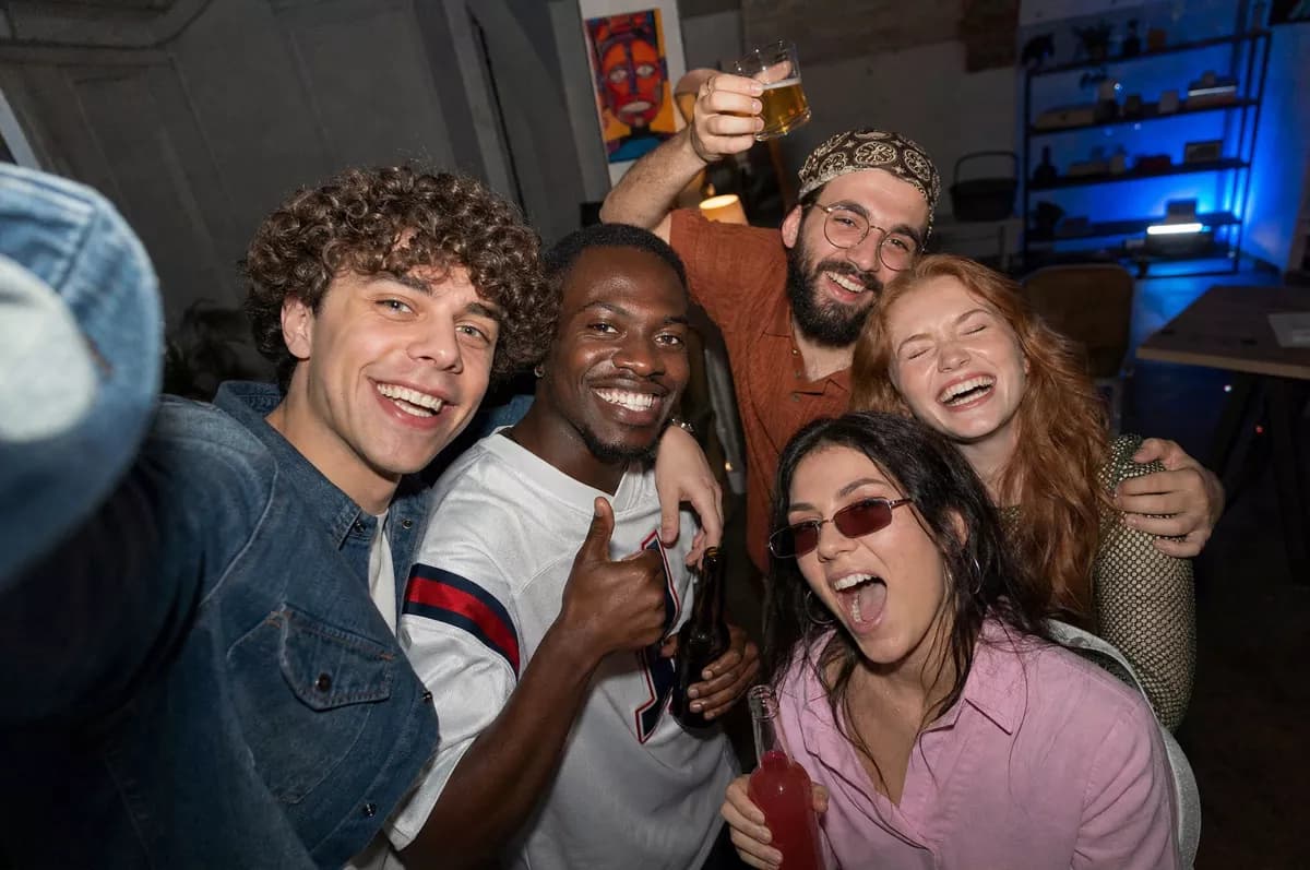 GPT Image 2 — People and lifestyle: A wide-angle group selfie of five friends at a house party, all laughing and cro