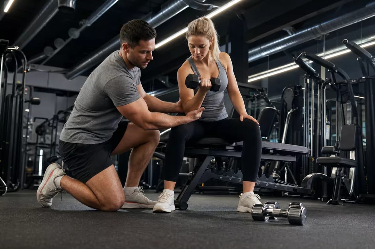 People and lifestyle: A gym scene: a muscular male trainer in a grey t-shirt and black shorts kneels o