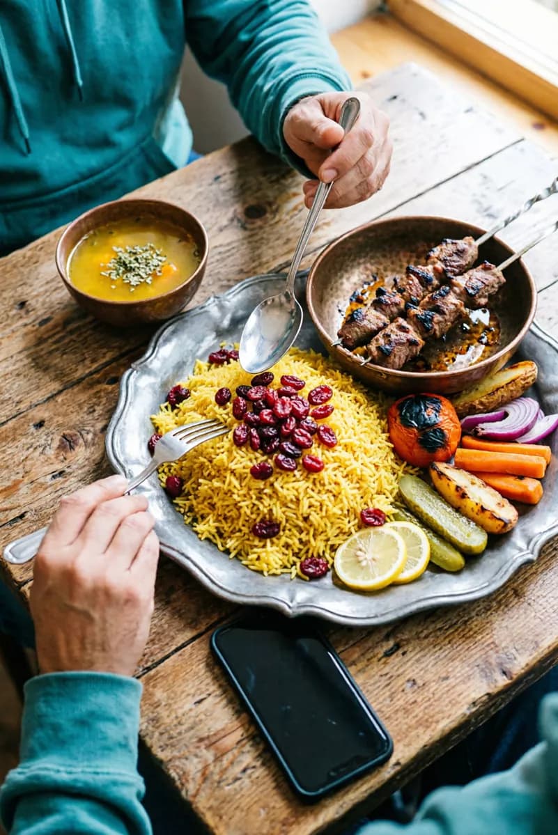 Food and beverage: A Persian meal on a rough wooden table, shot from above at an angle. A large sca