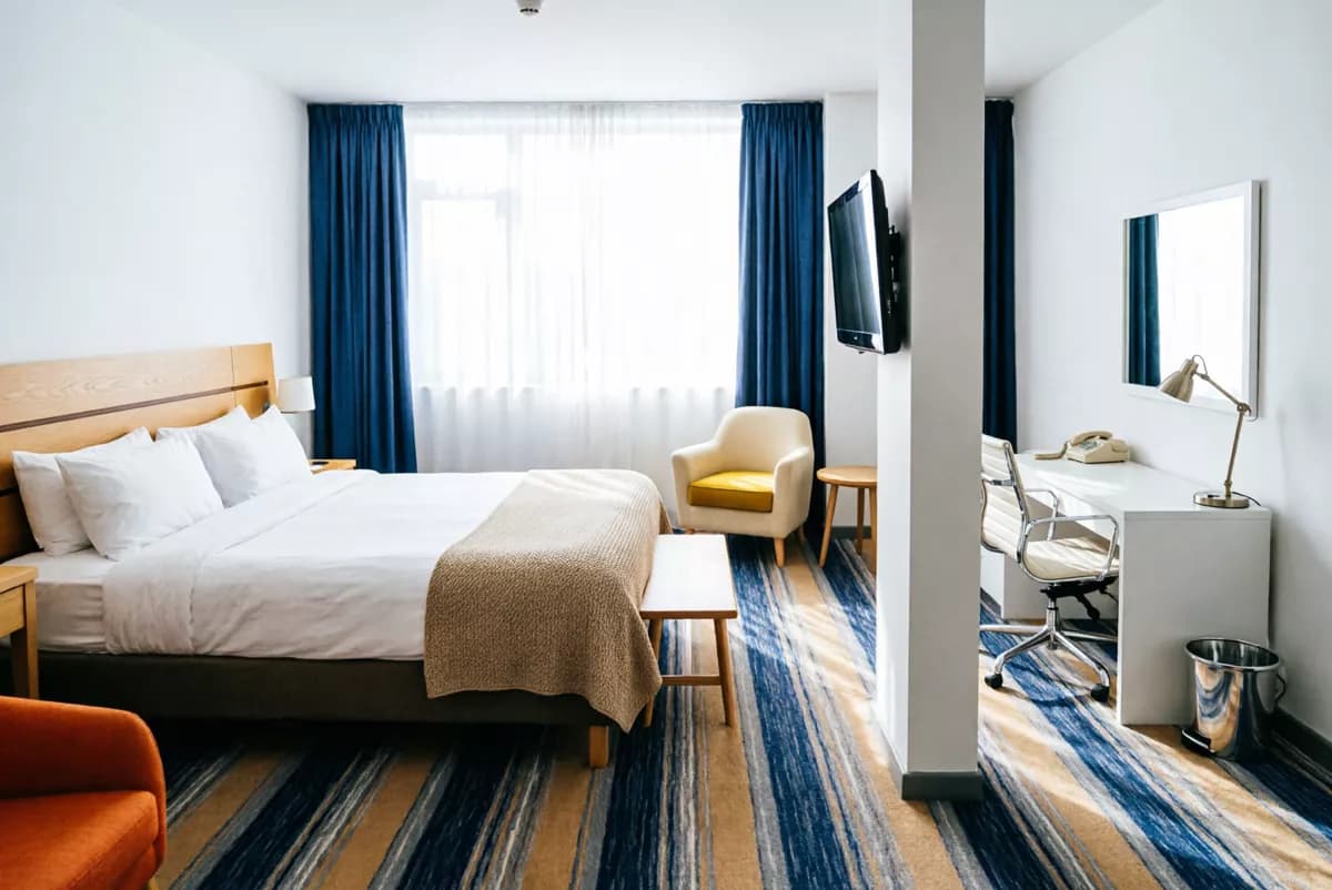 Qwen Image 2.0 — Interior: A spacious modern hotel room. A double bed with a pale wood slatted headboard, c