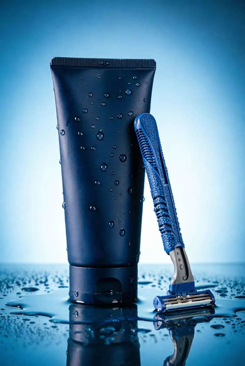 Product and e-commerce: A men's grooming product shot on a wet blue surface: a matte dark navy cosmetic 