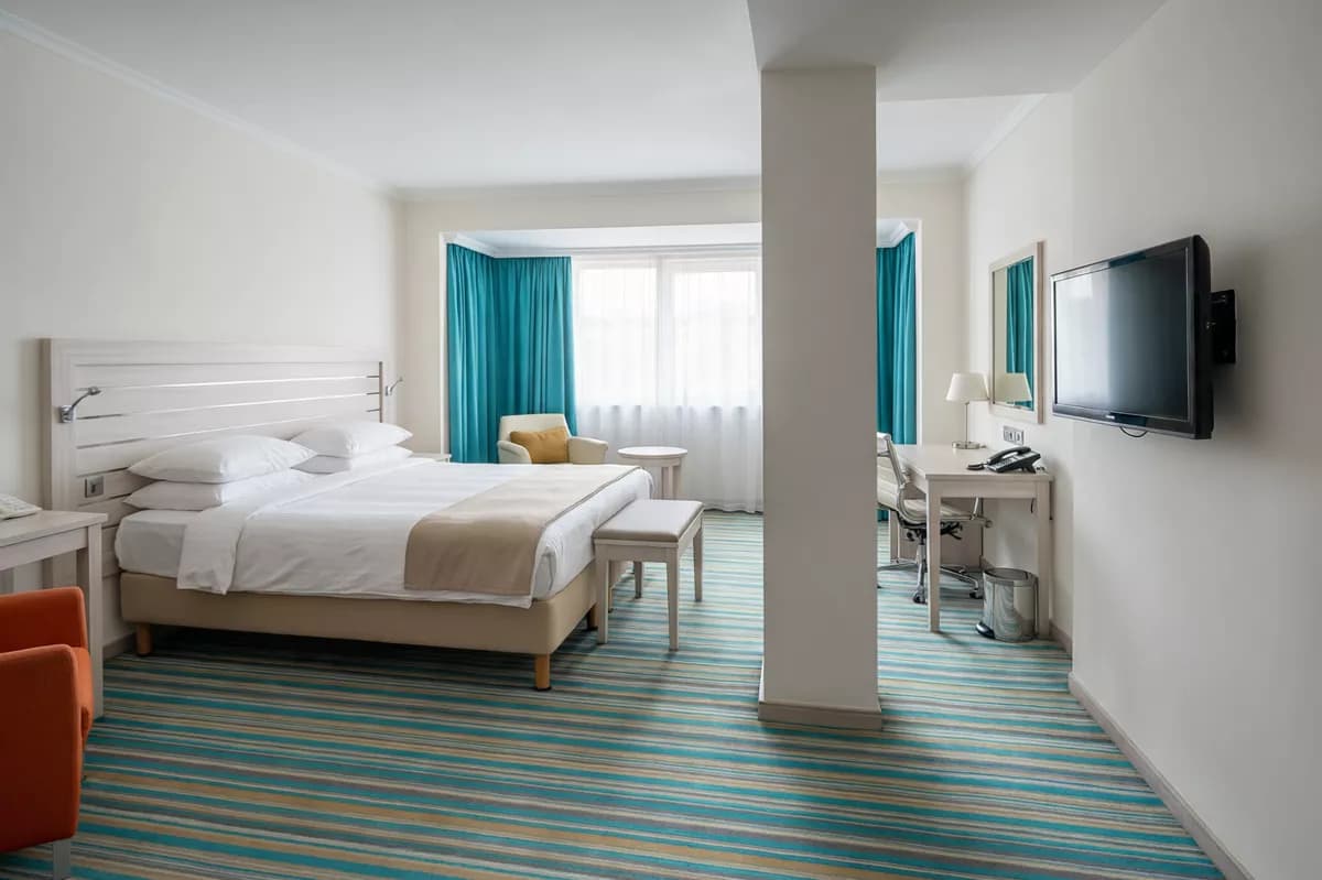 Interior: A spacious modern hotel room. A double bed with a pale wood slatted headboard, c