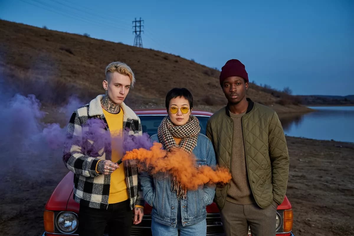 People and lifestyle: Three young people stand shoulder to shoulder in front of a red vintage sedan on