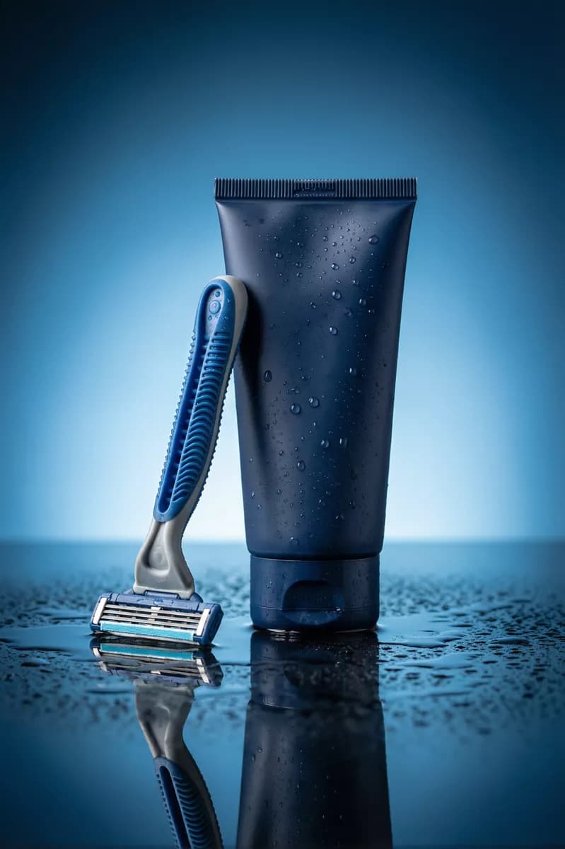 Product and e-commerce: A men's grooming product shot on a wet blue surface: a matte dark navy cosmetic 