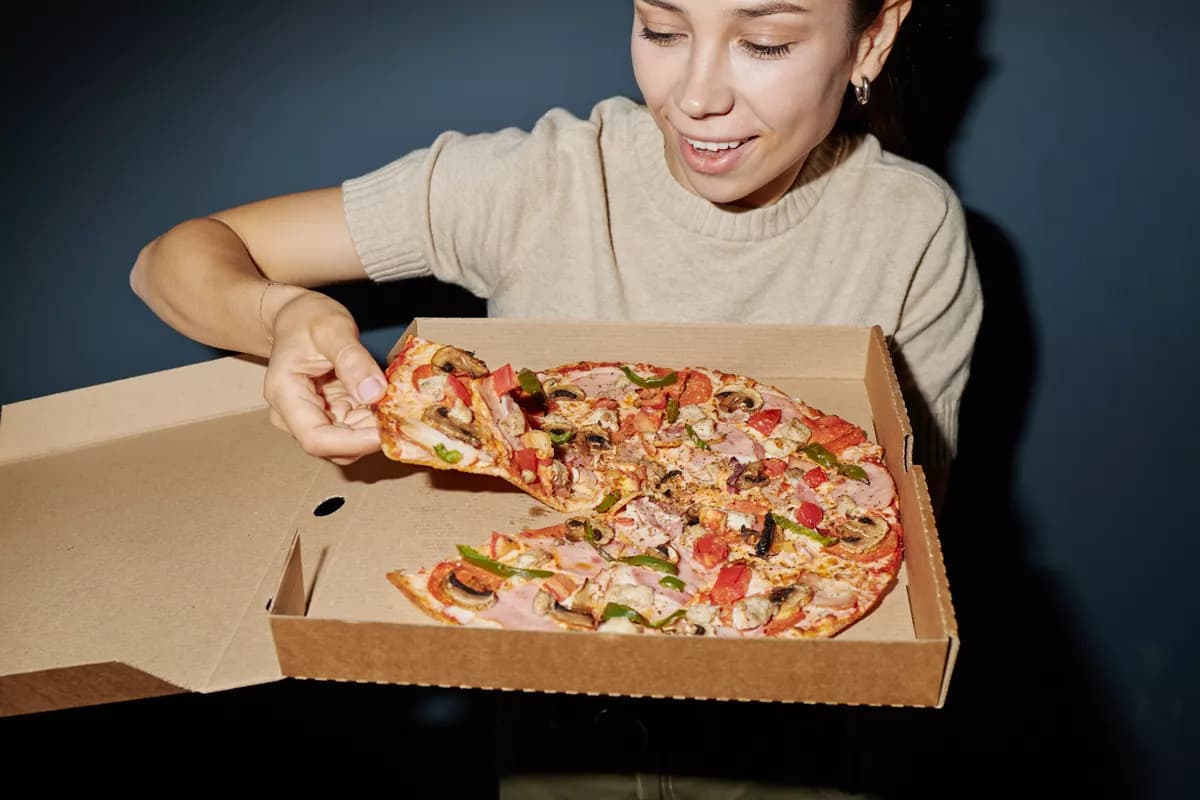 Real photograph — Food and beverage: A young woman with dark hair in a beige knitted t-shirt holds an open kraft card