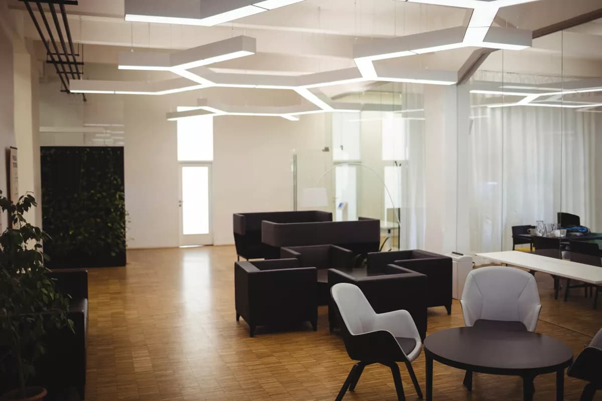 Real photograph — Interior: An open-plan office lounge. Overhead, a large angular ceiling installation of in