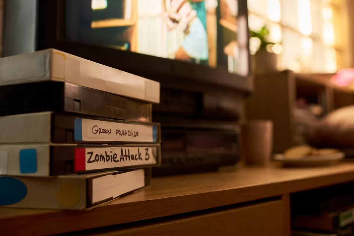 Real photograph — Layout and typography: A close-up of a stack of four VHS cassettes on a wooden media cabinet, shot alon