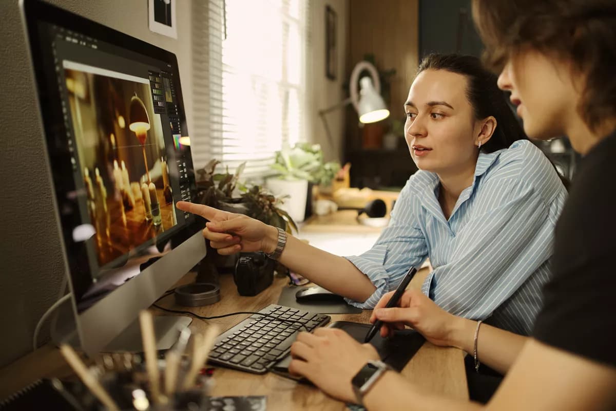 Real photograph — People and lifestyle: Two young women working together at a home-office desk. The one on the left, in 
