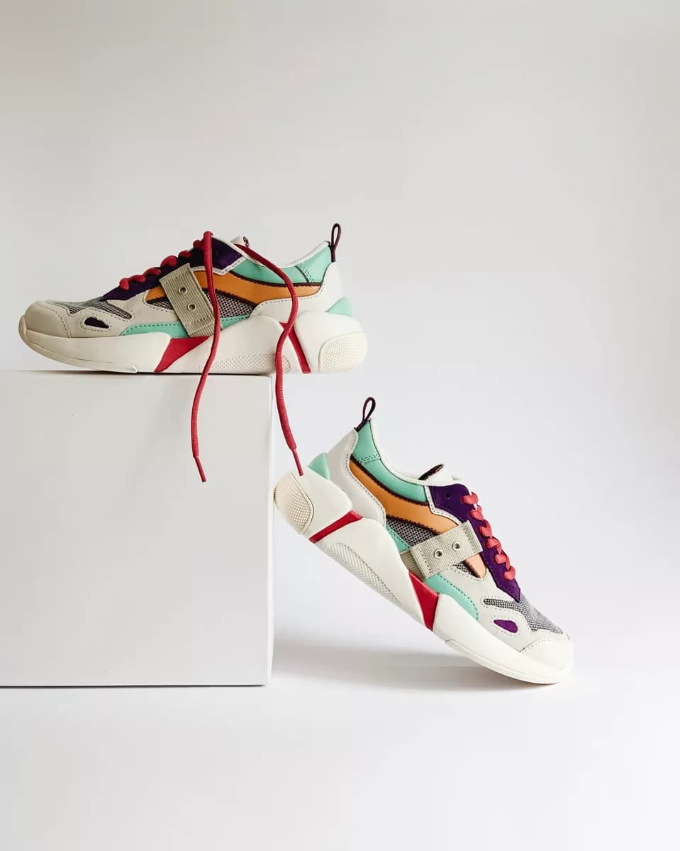 Real photograph — Product and e-commerce: Two chunky sneakers on a white seamless background with a white plinth. One rest