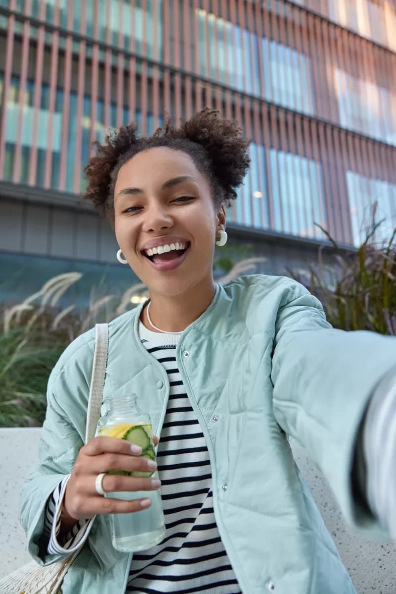 Real photograph — Social marketing: A low-angle outdoor selfie of a young woman with dark curly hair in two afro puf