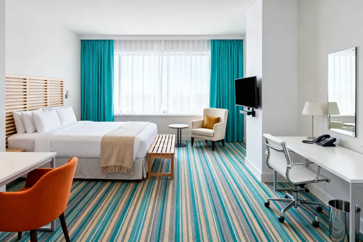 Interior: A spacious modern hotel room. A double bed with a pale wood slatted headboard, c
